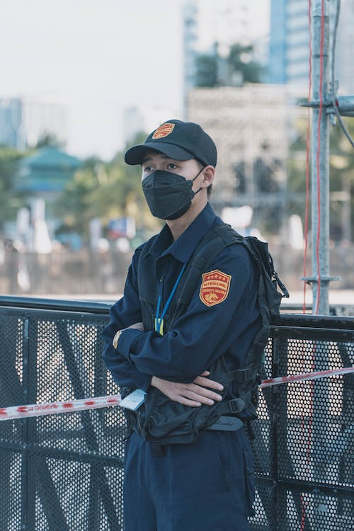 A security guard in uniform stands at his post with a lanyard and card around his neck